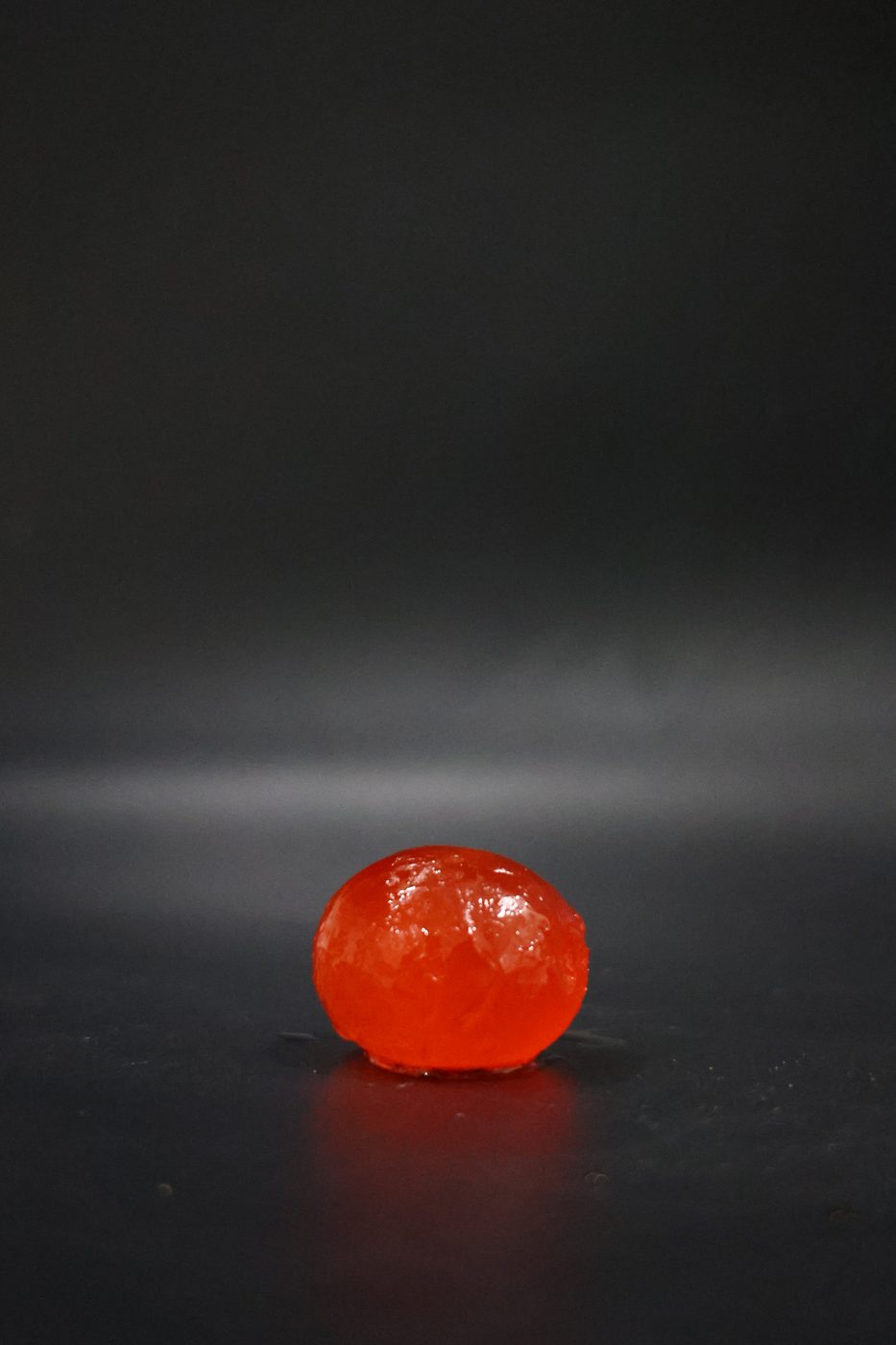 A single glistening round salted duck egg yolk on a dark surface